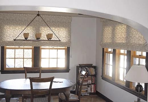 Cozy dining area with patterned Roman shades over wood-framed windows, showcasing custom window blinds, shades, and shutters Fullerton, CA homeowners choose for timeless style and light control.