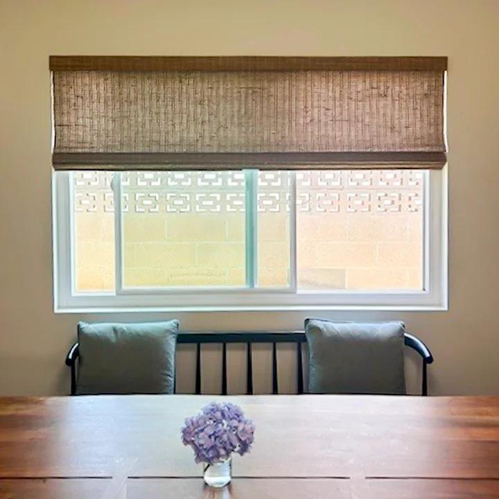 Dining area window with woven Roman shade providing soft light control, showcasing custom window blinds, shades, and shutters Placentia, CA homeowners choose for style and privacy.
