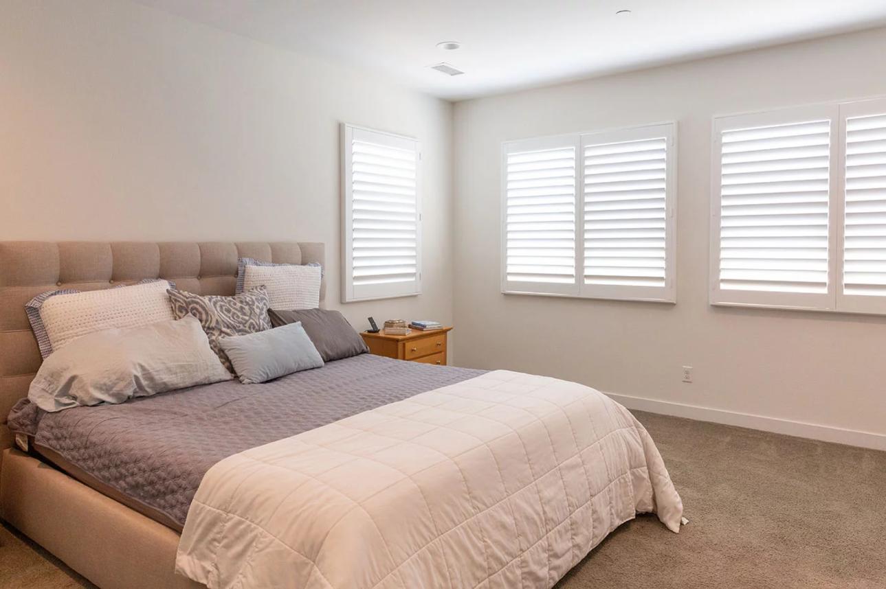 Bedroom with white plantation shutters, featuring window blinds, shades, and shutters Yorba Linda, CA for privacy and style.